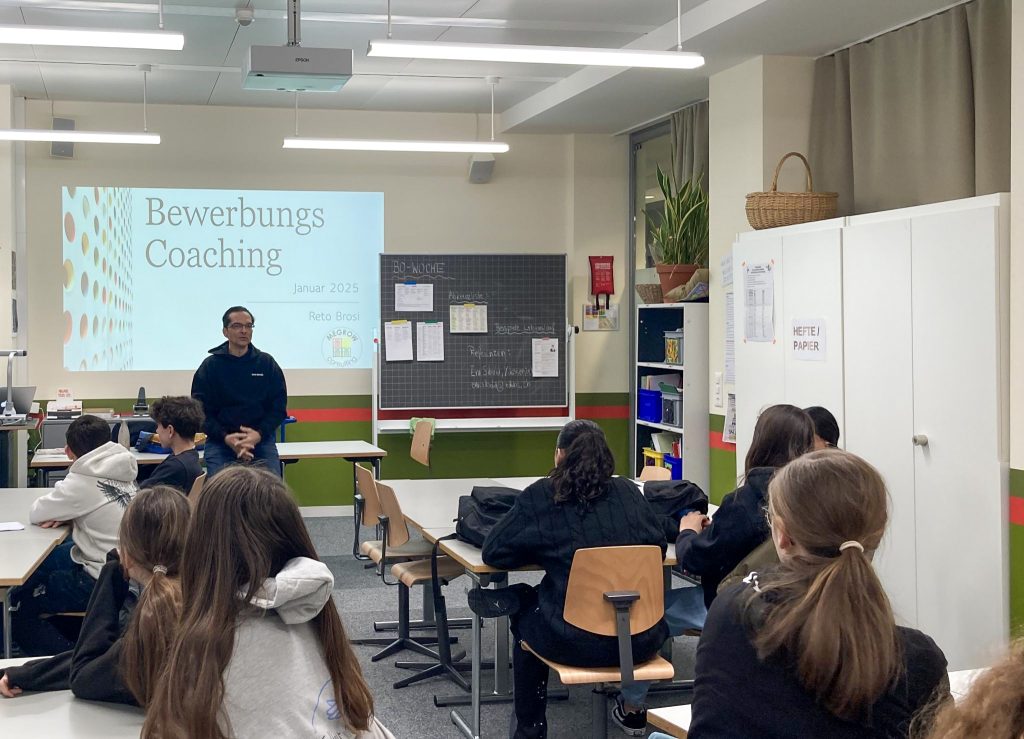 Ein Schulzimmer, Schüler und Schülerinnen, die Reto Brosi von der Megrow Consulting zuhoeren.